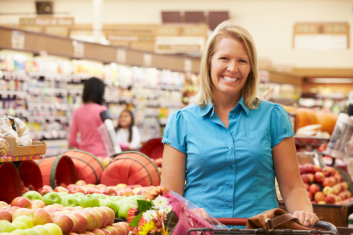 Woman Pushing Trolley By Fruit Counter In Supermarket Smiling To Camera