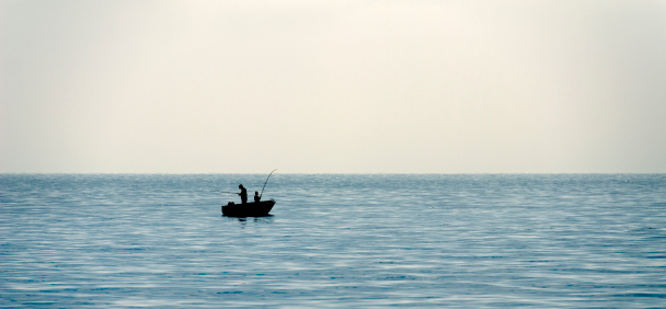 Silhouette of two fishermen (father and son) in boat on sea.