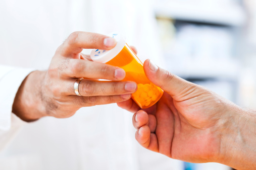 Close-up shot of pharmacist's or doctors hand giving a bottle of pills to senior male customer or patient at the drugstore.