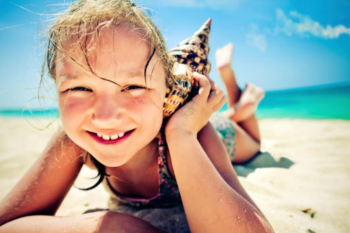 Little girl listening to the shell at the beach