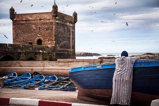 Ramparts of Skala de la Ville and an unrecognisable person(** Man's hat has been changed) leaning against a boat