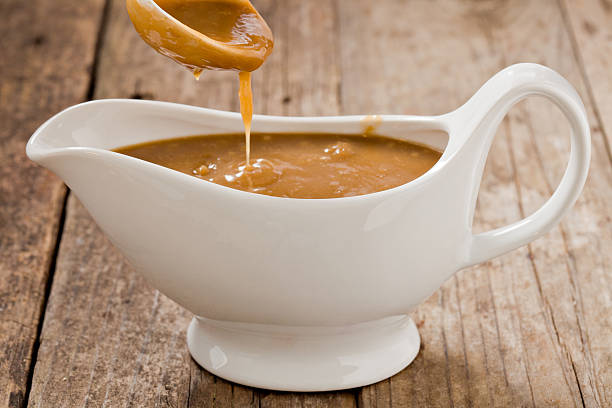 Pouring Gravy A close up shot of a small white ladle pouring brown gravy into a white ceramic gravy boat. Shot on a grungy old wooden table. savory sauce photos stock pictures, royalty-free photos & images