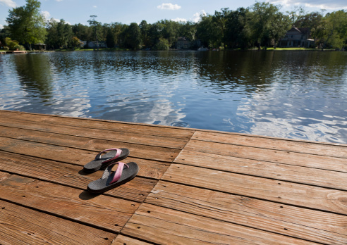 A pair of summer flip flops at the edge of a wooden dock on a public lake