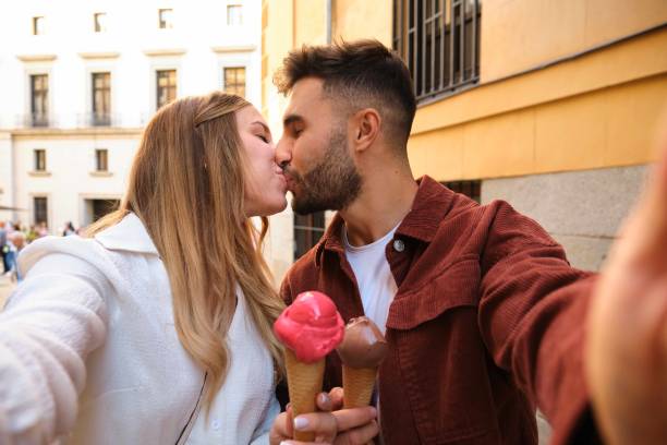 Happy young Caucasian couple taking a selfie while kissing with ice creams. Happy young Caucasian couple taking a selfie while kissing with ice creams at street. selfie madrid photos stock pictures, royalty-free photos & images