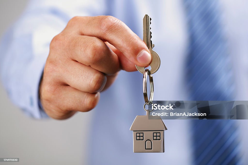 A man giving the key to a house Holding out house keys on a  house shaped keychain Passing - Giving Stock Photo