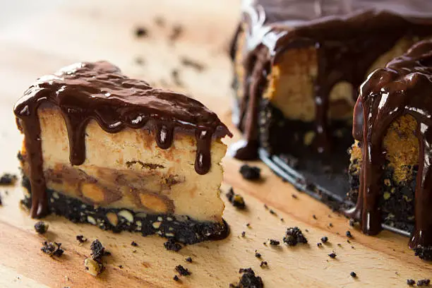 A peanut butter cheesecake with cookie crust and a chocolate ganache topping. Very narrow depth of field.