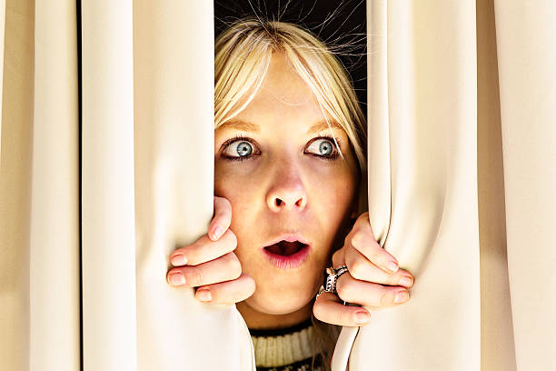 istock Shocked young blonde woman looking through closed drapes 174971956