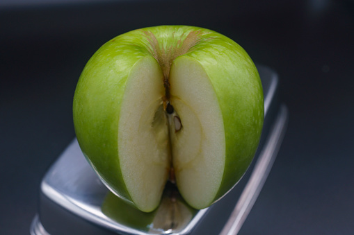 a sliced green granny apple with a piece on a black background top view
