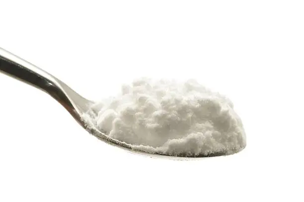"Bicarbonate of soda on a spoon, isolated on a white background."