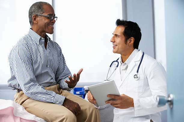 Doctor In Surgery With Male Patient Using Digital Tablet Doctor In Surgery With Male Patient Using Digital Tablet Smiling To Each Other. lab coat photos stock pictures, royalty-free photos & images