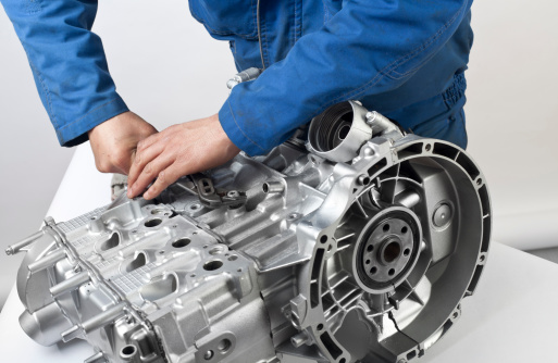 An asian mechanic is working on an new car engine wearing blue workwear.