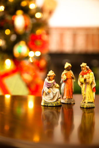 Three multi ethnic wisemen figurines  Christmas tree and fireplace background  Selective focus on kneeling wiseman. 