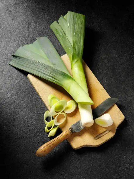 Leek vegetable on a wooden chopping board with a antique knife on a dark slate background.Click on the link below to see more of my fruit and vegetable images