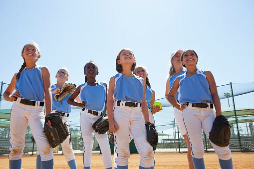 Multi-ethnic girls softball team standing on ball field (7 to 10 years).