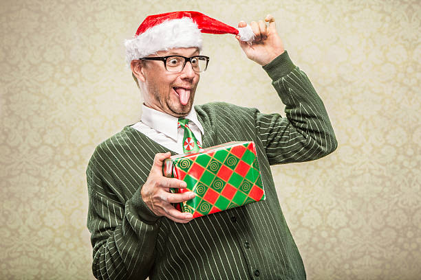 Silly Dad Nerdy Christmas Man holding wrapped gift A dorky nerd man in cardigan sweater holding holiday christmas gift. He is wearing a santa hat and a holiday festive neck tie. christmas nerd sweater cardigan stock pictures, royalty-free photos & images