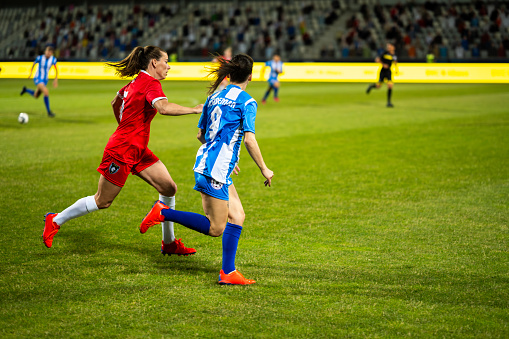 Female football players running on field during match, full length shot