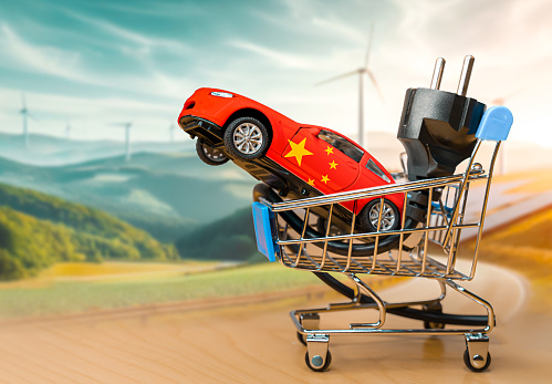 Toy car painted with tue flag of china and electrical plug inside a small shopping cart. Concepts about the leadership of China in the global electric car market and growht of sales of EV.