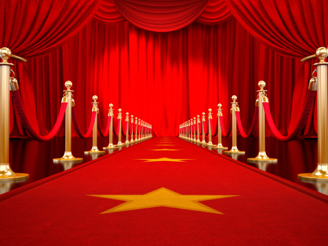 Red carpet with gold stanchions and velvet ropes leading to the stage with red curtains illuminated by spotlights..Similar images: