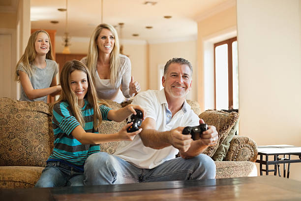 Happy Caucasian family of four having fun playing videogames Happy Caucasian family of four having fun playing videogames at home teenager couple child blond hair stock pictures, royalty-free photos & images