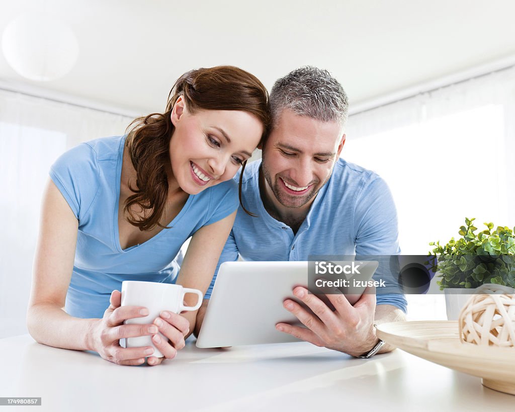 Happy Couple with digital tablet Close up of a happy couple standing at the table at home and using digital tablet. 25-29 Years Stock Photo