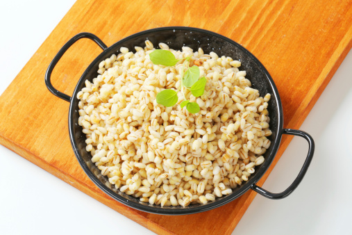 pile of cooked peeled barley with a basil in a black metal pot on a wooden cutting board