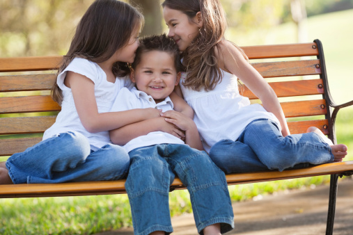 Portrait of cute little boy with two sisters sitting on park bench