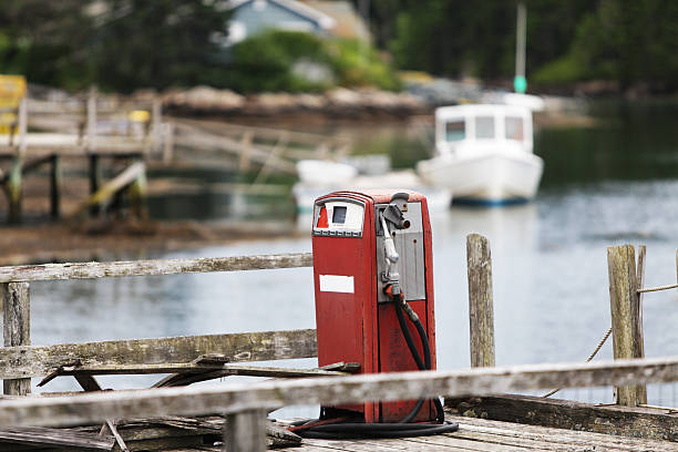 This obsolete marine gasoline fuel pump hasn't been used in decades. It sits rusting away on a rickety, rotting wooden dock in a small cove along the coastline of Maine, USA. Despite featuring many similar ancient relics, this New England harbor bustles with commercial lobster boats, sailboats and personal/pleasure fishing boats of all sizes throughout the summer months.