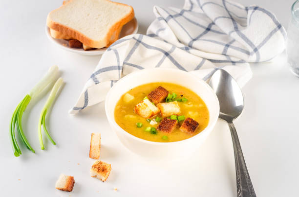 Split pea soup with croutons and green onion in a bowl on white table. Healthy homemade thick soup in white bowl for winter lunch.