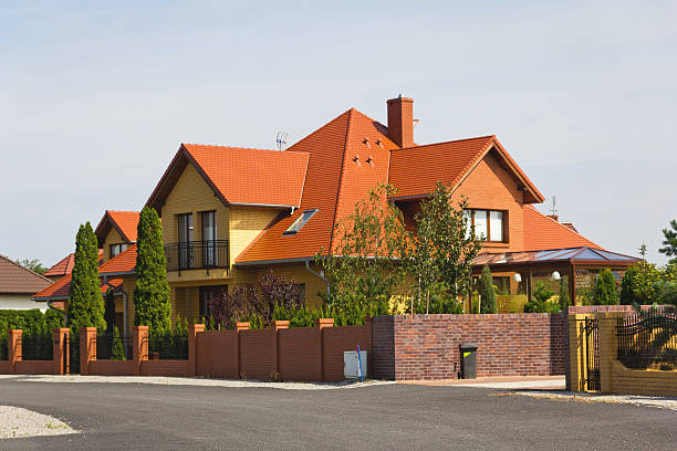 Front view of facade exterior made of brown brick in a sunny day. Close up of two white windows with amber curtains and colorful leaves in front