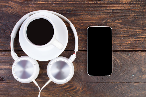 Headphones, mobile phone, idiobook, coffee cup on a wooden table. The concept of leisure and learning, hobby. Listen to music, literature. Top view with copy space