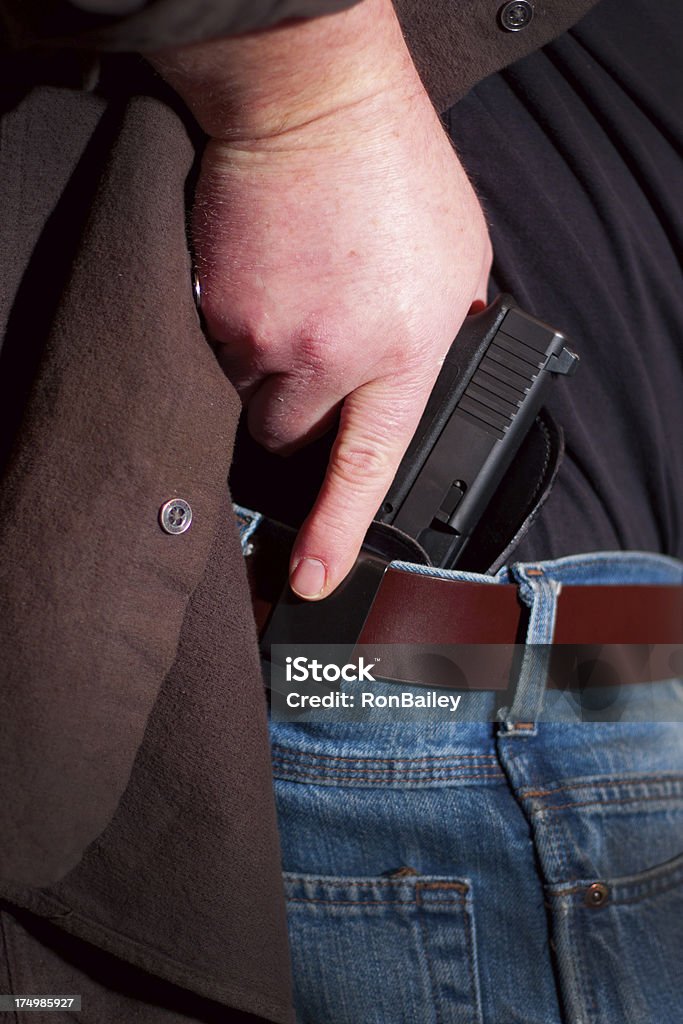 Concealed Carry Firearm Drawn From an Inside-the-Waistband Holster A caucasian man drawing his modern polymer pistol from an IWB (inside the waistband) holster under his loose outer shirt.All images in this series... Carrying Stock Photo