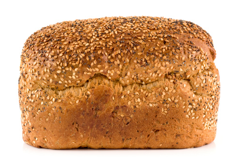 Seeded loaf of whole wheat bread on a white background.