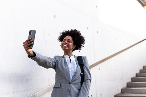 African businesswoman gesturing success while taking a selfie standing outdoors