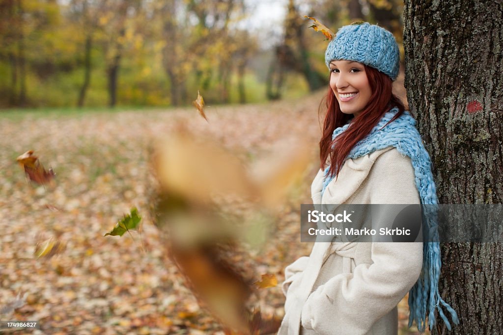 Girl leaning on tree in the park with falling leaves girl leaning on a huge tree in the autumn forest, in warm clothes, smiling and posing. Falling leaves also captured. 20-29 Years Stock Photo
