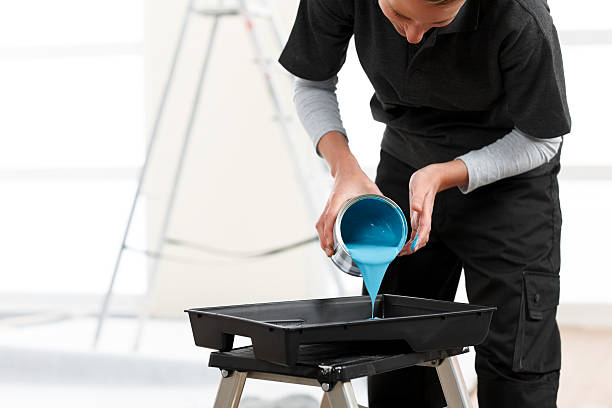 Woman painter pouring blue color paint into roller pan