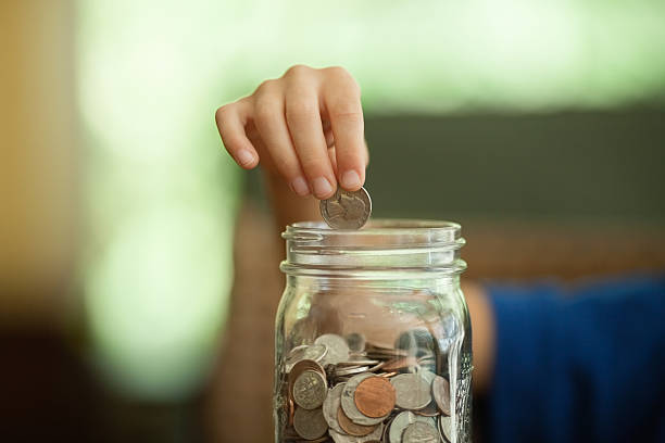 istock Boy's Hand Dropping Coin Into Money Jar 174987609