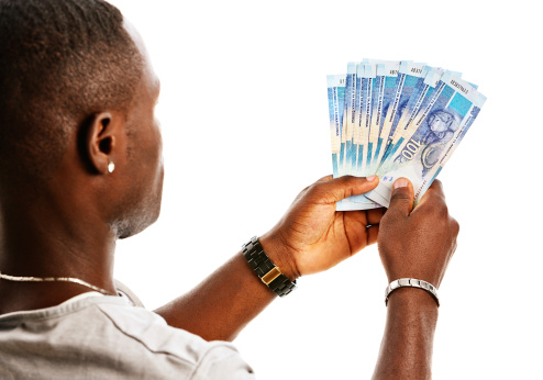 Looking over the shoulder of a man holding a bundle of the new South African One Hundred Rand notes featuring the iconic statesman Nelson Mandela.