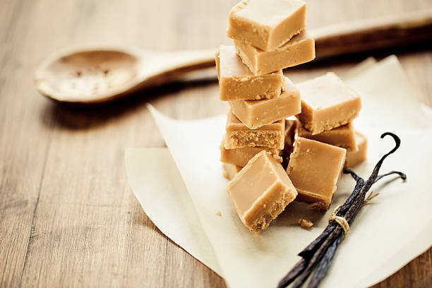Stacks of square vanilla fudge over a wooden spoon and table Caramel fudge cubes. Fudge stock pictures, royalty-free photos & images