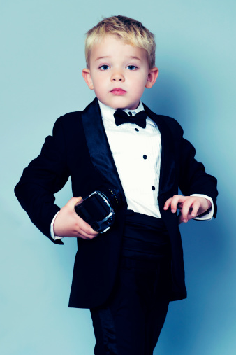 Little boy in a tuxedo turns his head and looks surprised. He is hold an old retro camera in his right hand.