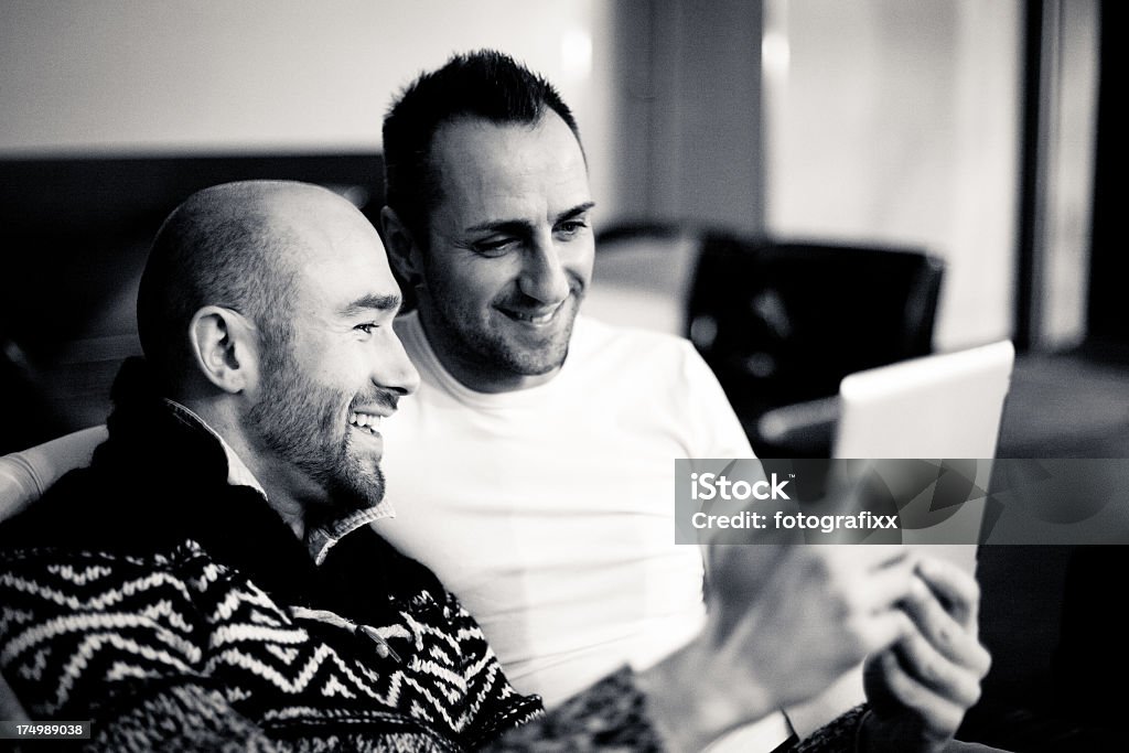 gay couple sitting arm in arm and using digital tabletamorous couple using digital tablet homosexual couple sitting arm in arm and using digital tablet Adult Stock Photo