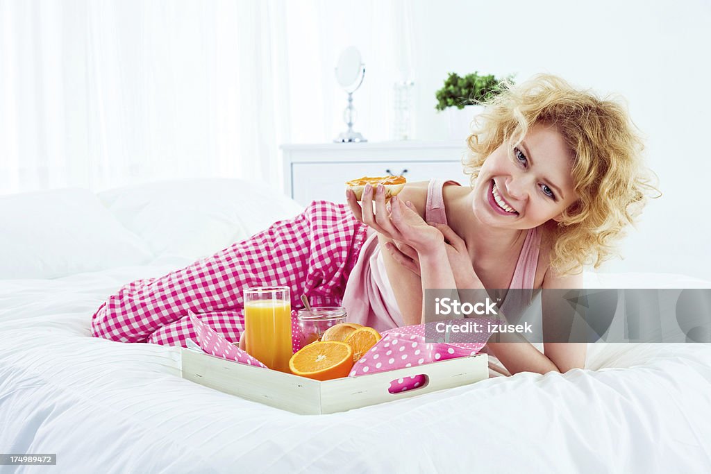 Healthy breakfast in a bed Happy young woman lying on a bed in bedroom and eating breakfast. 25-29 Years Stock Photo
