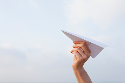 Woman’s hand launching white paper airplane outdoors.