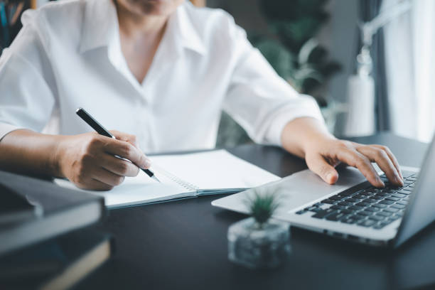 istock Student studying online course via laptop and lecture on notepad. Business planning, E learning concept. Casual business woman writing on notebook and working on laptop computer in modern office. 1749908717
