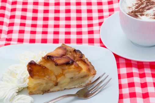 A slice of fresh baked apple tart served with a coffee.   In Germany this is known as Kaffee und kuchen.