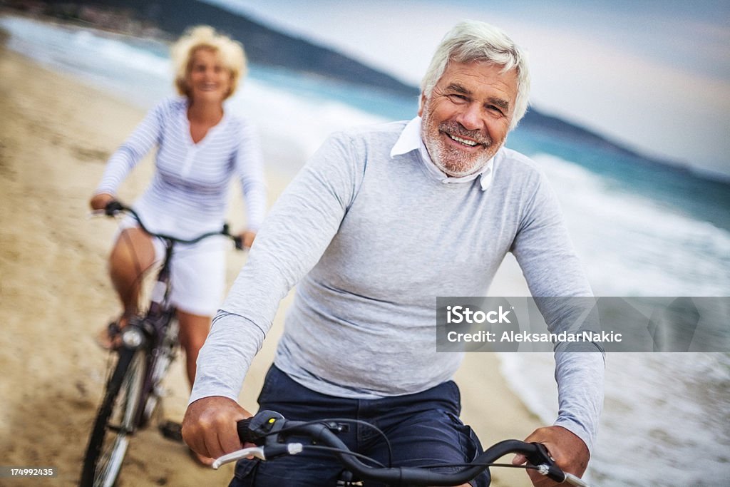 Active seniors Senior couple driving bicycles on the beach Exercising Stock Photo