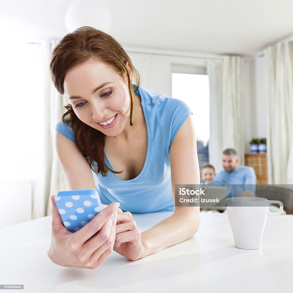 Woman with smart phone Close up of a woman using smart phone, while her husband and son using laptop in the background. 25-29 Years Stock Photo