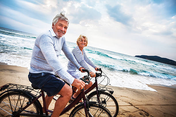 senior actifs - senior couple cycling beach bicycle photos et images de collection