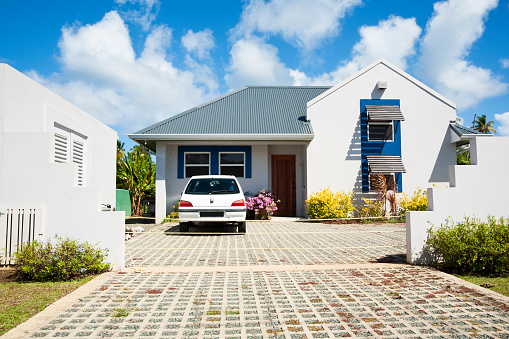 A modern style Caribbean Home with a car in the driveway and under a blue cloudy sky.