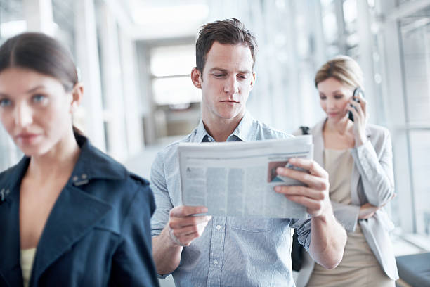 Reading the newspaper while he waits Attractive young businessman reading the paper while in a queue newspaper airport reading business person stock pictures, royalty-free photos & images