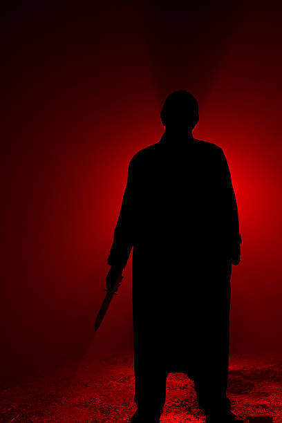 Silhouette of a psycho killer with a knife on red Dark, foggy outdoor silhoette of a man wearing a knit cap and trenchcoat, weilding a large knife. creepy stalker stock pictures, royalty-free photos & images